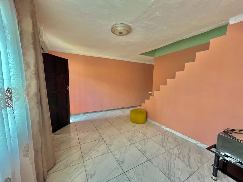 An empty living area featuring tiled flooring and an integrated staircase, offering a blank canvas for interior design updates.