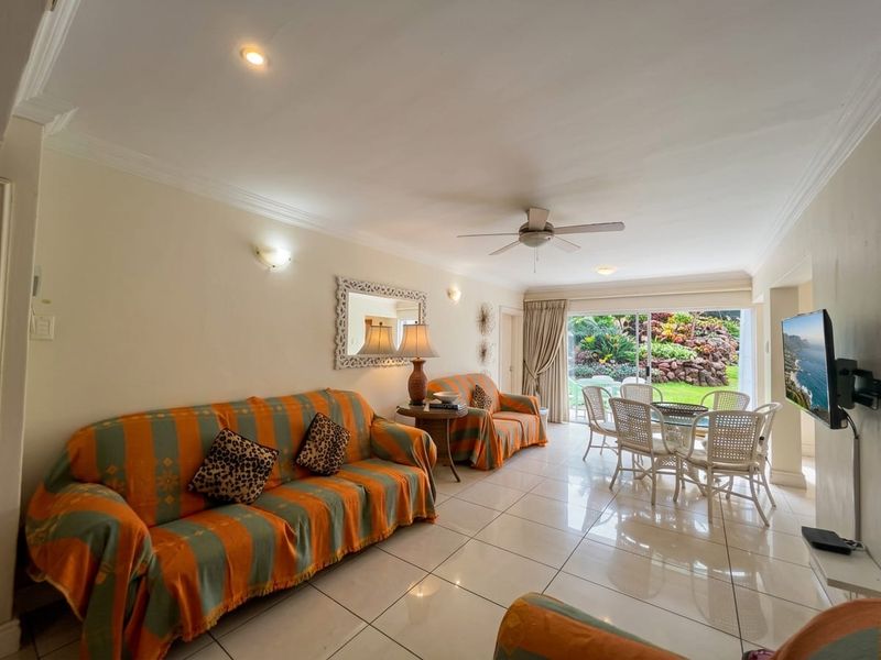Open-plan living and dining area featuring tiled floors, ceiling fan, and large sliding glass doors providing direct access to the garden.