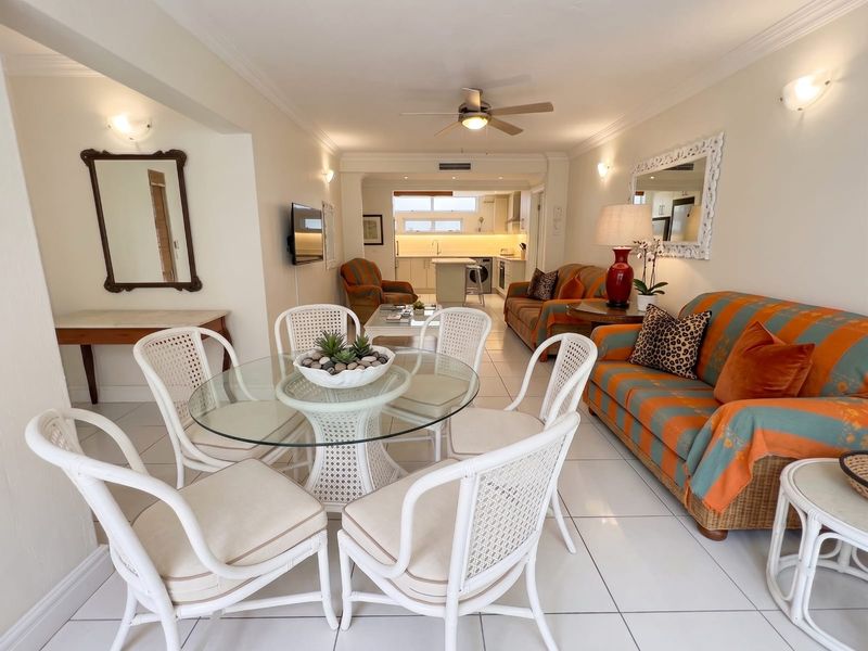 Open-plan living and dining area featuring tiled floors, ceiling fan, and a connected kitchen with built-in cabinetry and appliances.