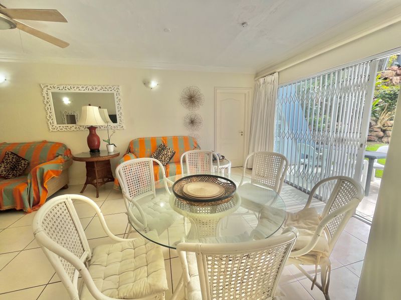 A living and dining area featuring tiled flooring, a ceiling fan, and sliding glass doors leading to an outdoor space with security gates.