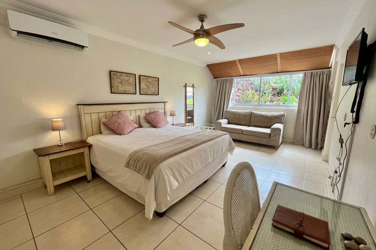 Spacious bedroom featuring tiled flooring, a ceiling fan, and a wall-mounted air conditioning unit, offering a comfortable and functional living space.
