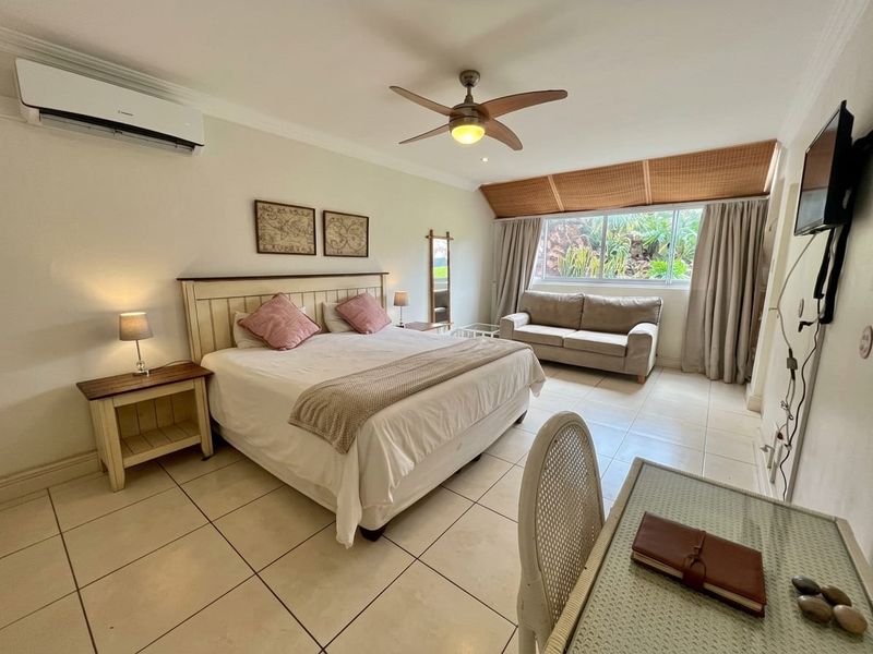 Spacious bedroom featuring tiled flooring, a ceiling fan, and a wall-mounted air conditioning unit, offering a comfortable and functional living space.