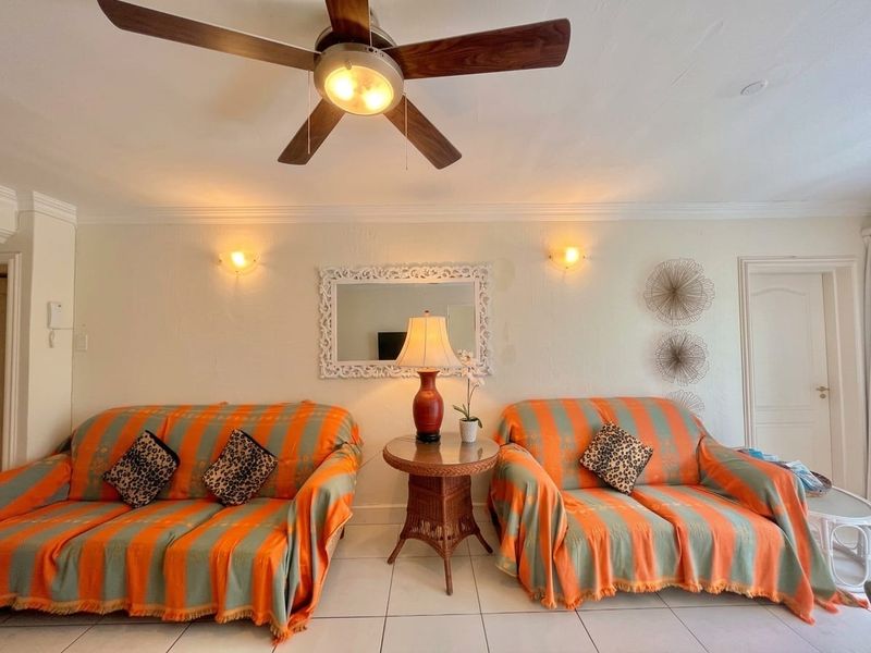 A living room featuring tiled flooring, crown molding, a ceiling fan, and wall-mounted lighting fixtures.