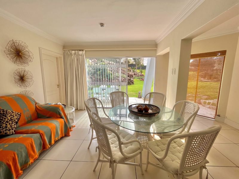 Bright open-plan living and dining area featuring tiled floors, crown molding, and large sliding glass doors providing direct access to the garden.