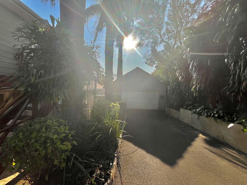 A view of the property driveway leading to a garage, framed by mature trees and landscaping.