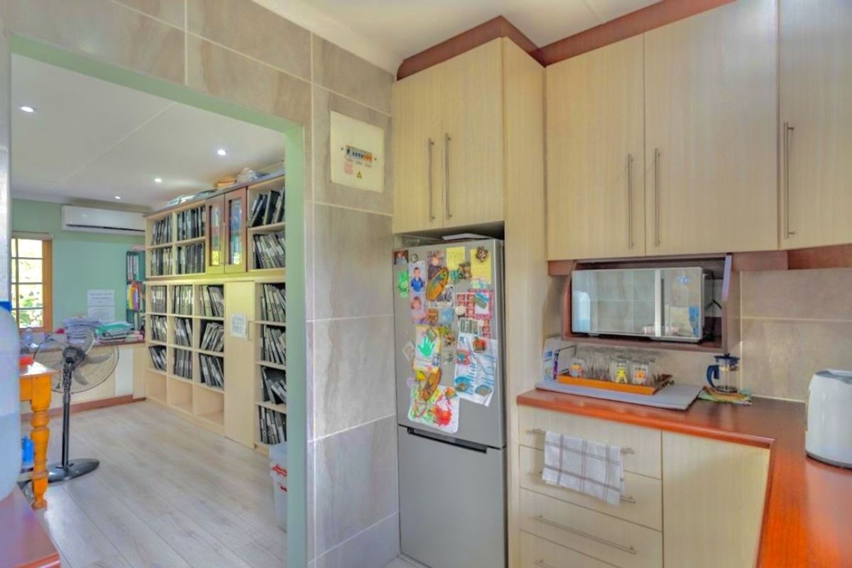 A functional kitchen featuring light wood-finish cabinetry, laminate countertops, and a built-in microwave, with an open transition to an adjacent study or living area.