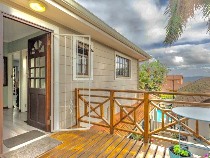 A raised timber balcony featuring a wooden balustrade and security gate, providing an elevated outdoor space with views of the surrounding property.