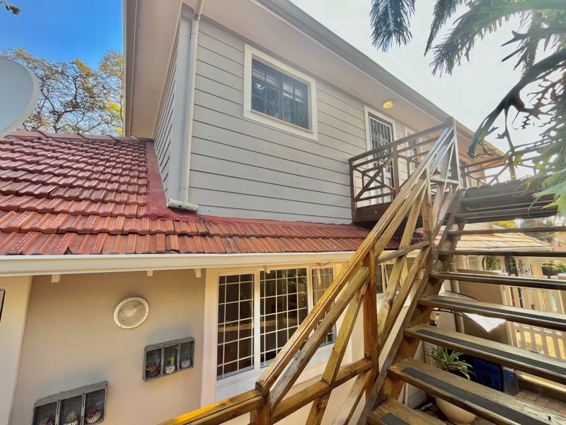 Rear exterior view of the property featuring a timber staircase leading to an upper-level balcony, terracotta roof tiles, and weatherboard cladding.