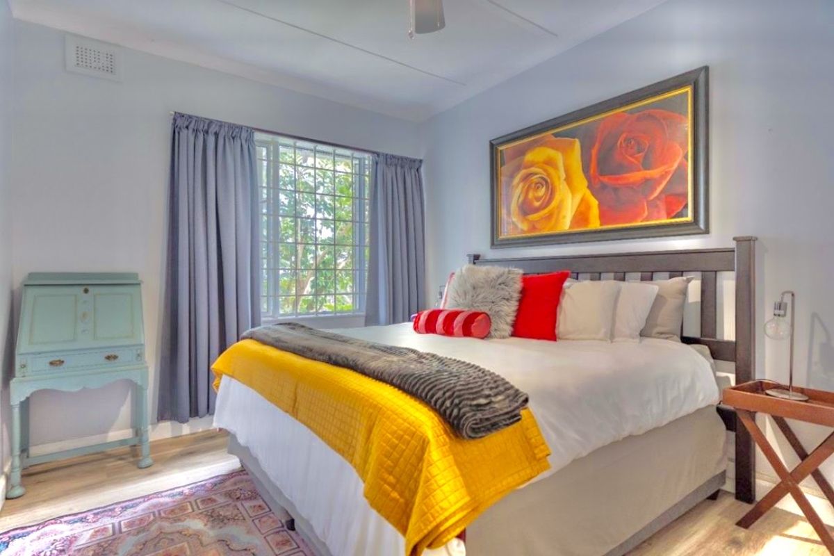 A well-lit bedroom featuring laminate flooring, a ceiling fan, and a window fitted with security bars.