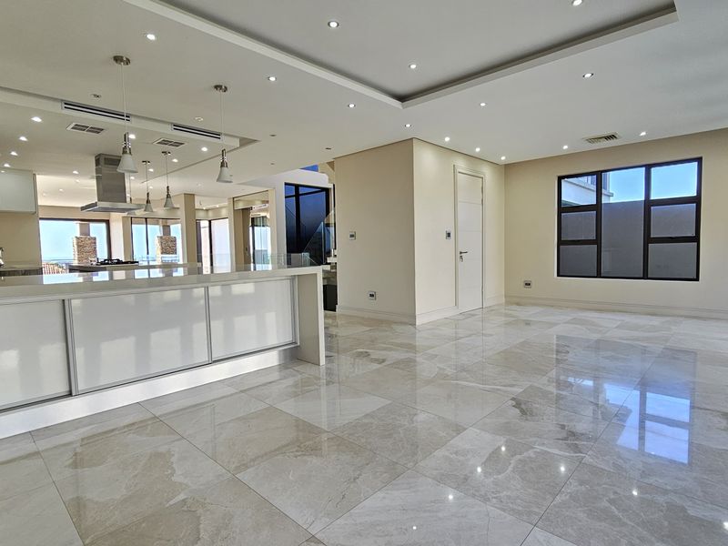 Spacious open-plan living and kitchen area featuring high-gloss cabinetry, stone countertops, large-format porcelain tiles, and modern recessed lighting throughout.