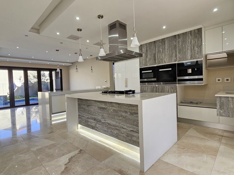 Modern open-plan kitchen featuring a large island, high-end built-in appliances, stone countertops, and seamless access to the outdoor area through bi-fold doors.