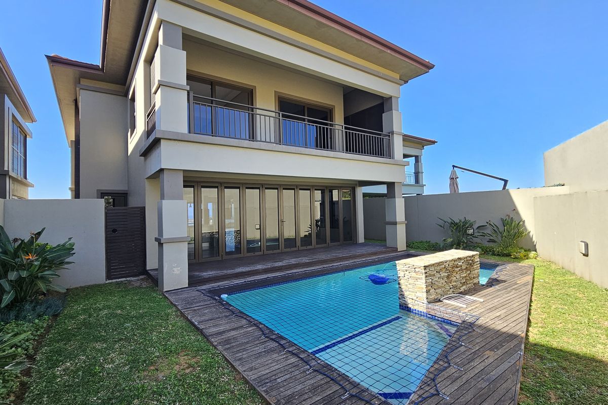 Rear exterior view of a townhouse featuring a swimming pool, timber decking, covered patio, and an upper-level balcony with stacking doors.
