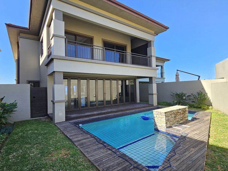 Rear exterior view of a townhouse featuring a swimming pool, timber decking, covered patio, and an upper-level balcony with stacking doors.