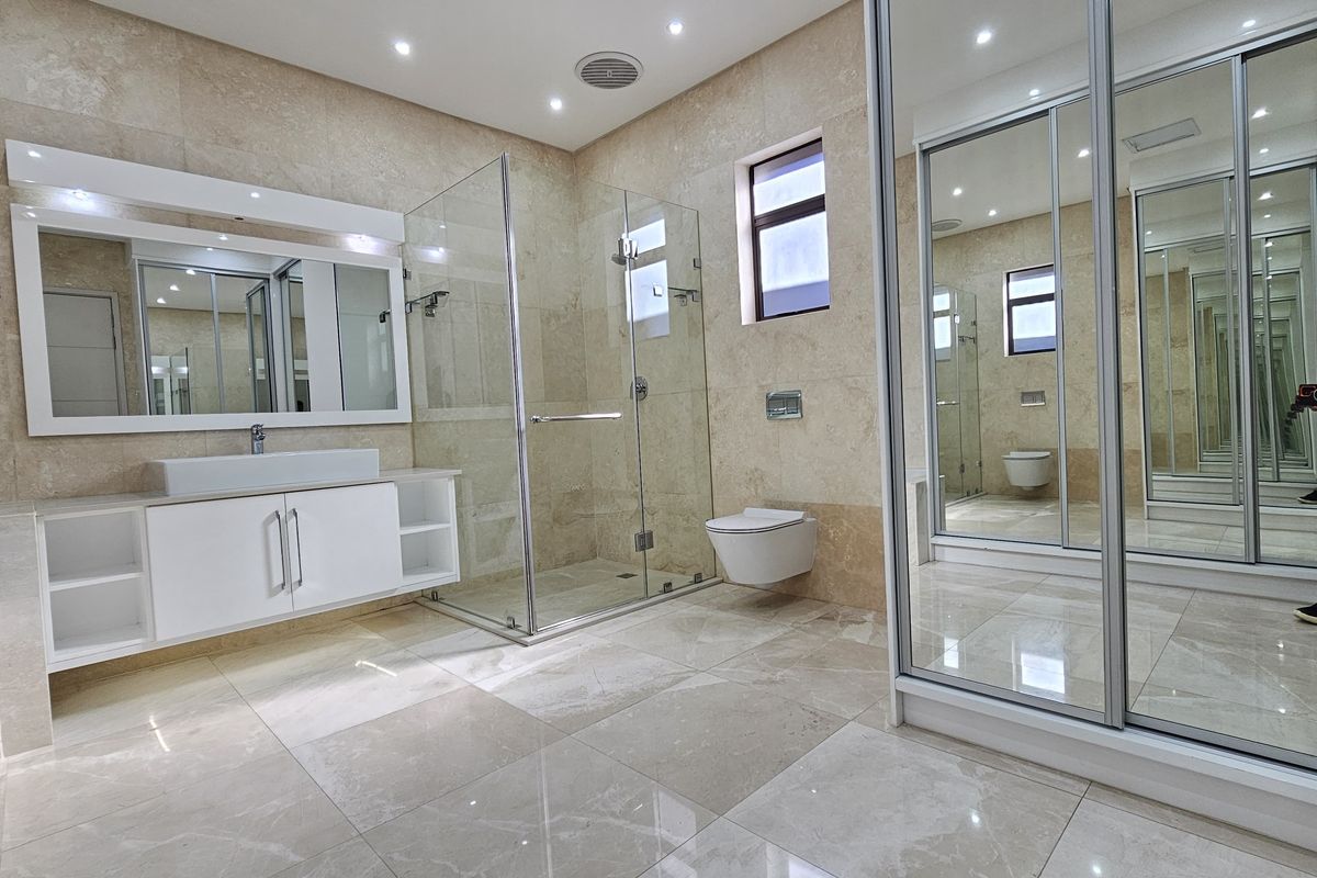 Modern, spacious bathroom featuring high-end travertine wall tiling, a wall-mounted vanity with vessel sink, glass shower enclosure, and wall-hung toilet.