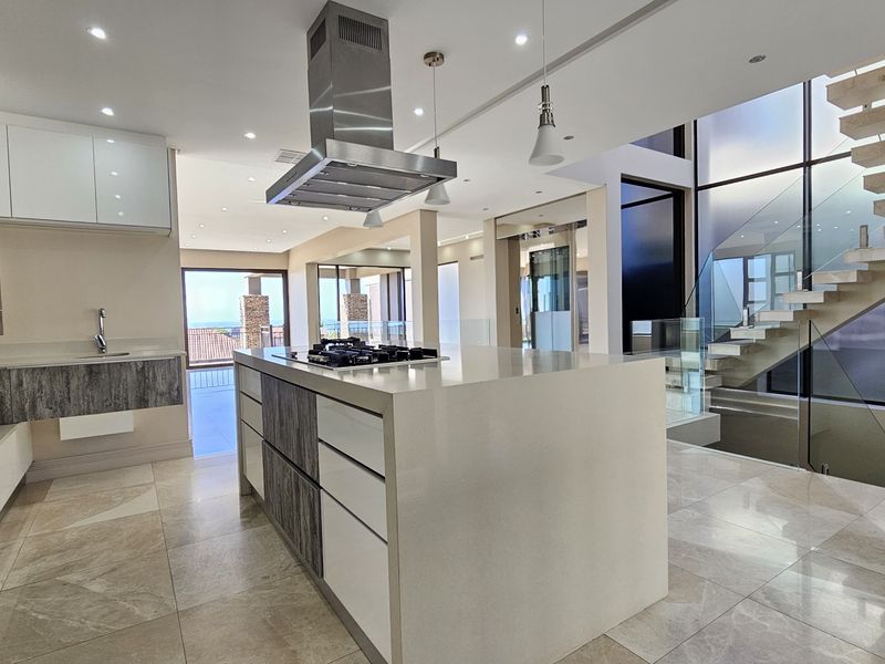 Modern open-plan kitchen featuring a central island with gas cooktop, high-end built-in appliances, and a striking floating staircase with glass balustrade.