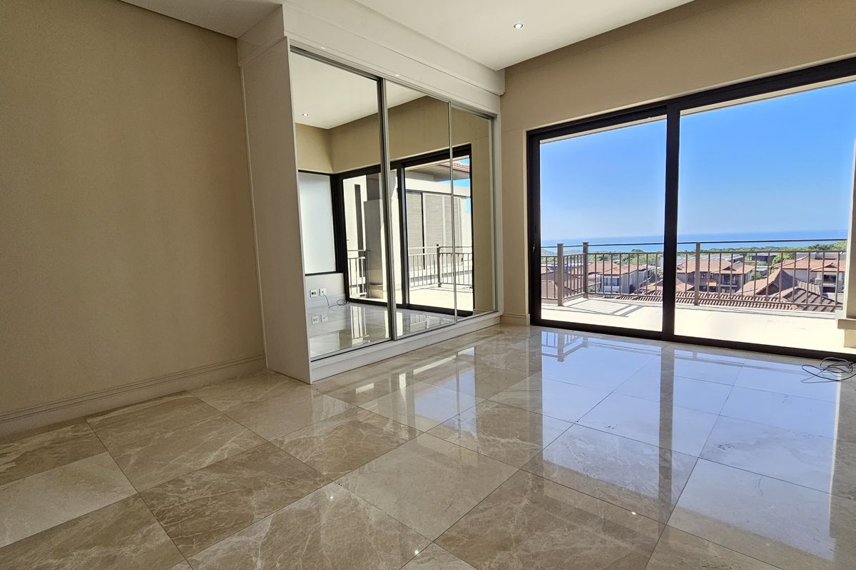 Spacious bedroom featuring polished tiled floors, a large built-in mirrored wardrobe, and sliding glass doors opening to a balcony with scenic views.