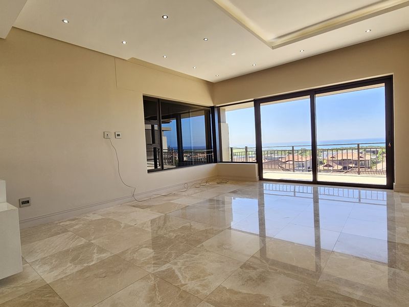 Spacious, light-filled living area featuring polished marble flooring, recessed ceiling lighting, and large sliding glass doors opening to a balcony with coastal views.