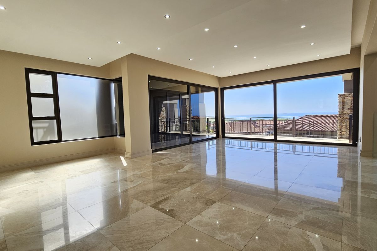 Spacious, light-filled living area featuring large format polished floor tiles, recessed downlighting, and expansive sliding glass doors opening to a scenic balcony view.