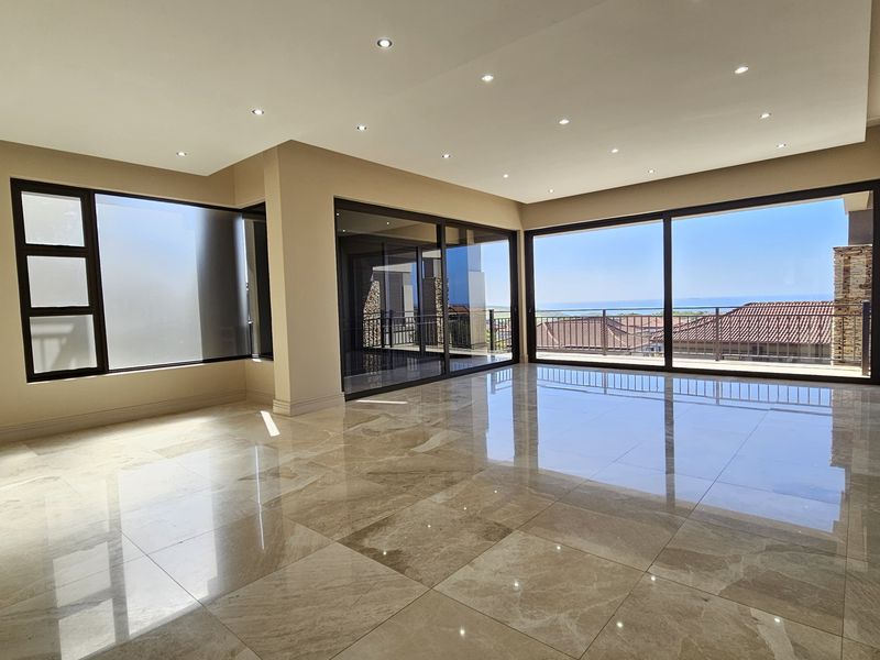 Spacious, light-filled living area featuring large format polished floor tiles, recessed downlighting, and expansive sliding glass doors opening to a scenic balcony view.
