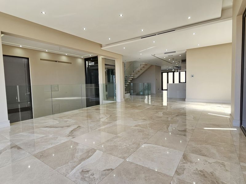 Spacious open-plan living area featuring high-end marble flooring, recessed lighting, and a modern glass balustrade, offering a bright and contemporary interior space.