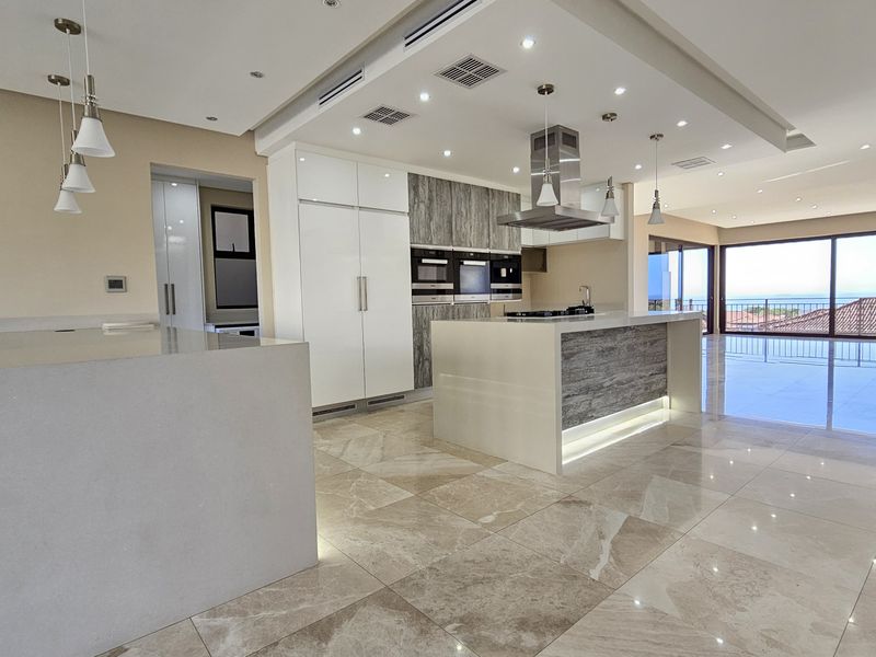 Modern open-plan kitchen featuring a large island, high-end built-in appliances, stone countertops, and polished porcelain flooring, flowing seamlessly into the living area with ocean views.