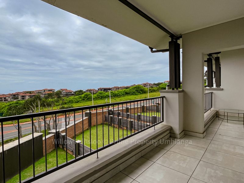 A spacious covered balcony featuring tiled flooring and a metal balustrade, offering elevated views of the surrounding neighborhood and landscape.