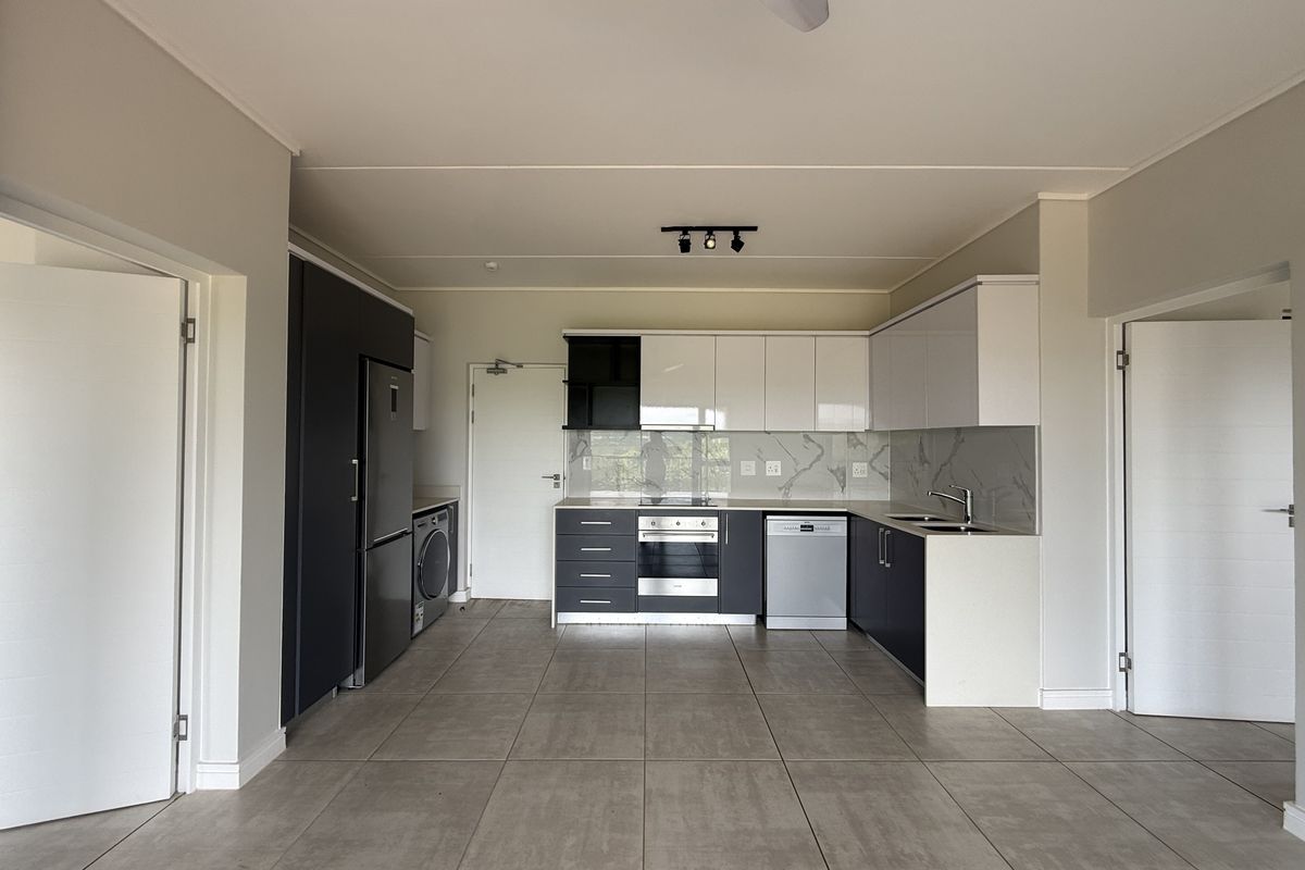 Modern, clean-lined kitchen featuring high-gloss cabinetry, stone countertops, integrated appliances, and neutral tiled flooring in an open-plan layout.