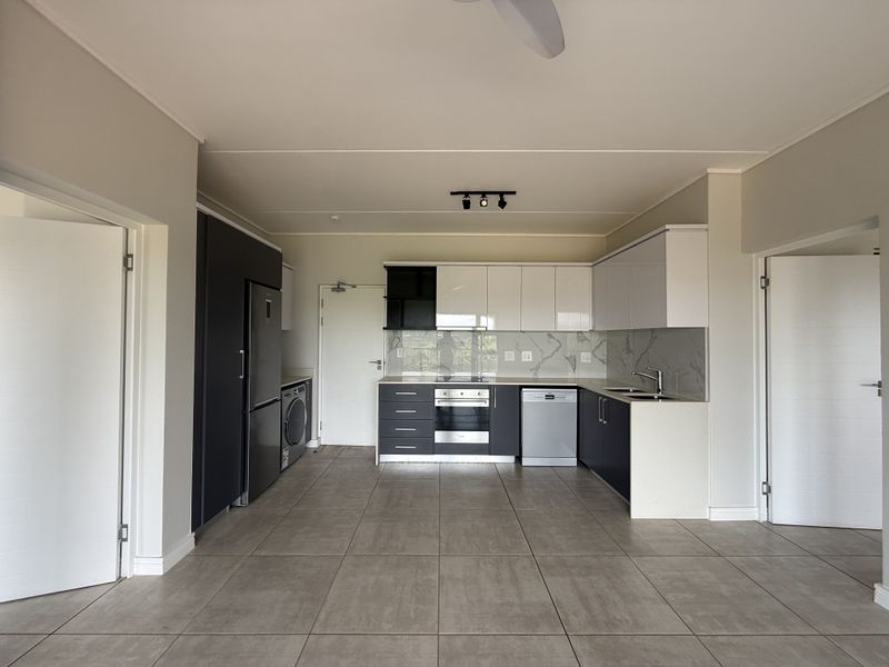 Modern, clean-lined kitchen featuring high-gloss cabinetry, stone countertops, integrated appliances, and neutral tiled flooring in an open-plan layout.