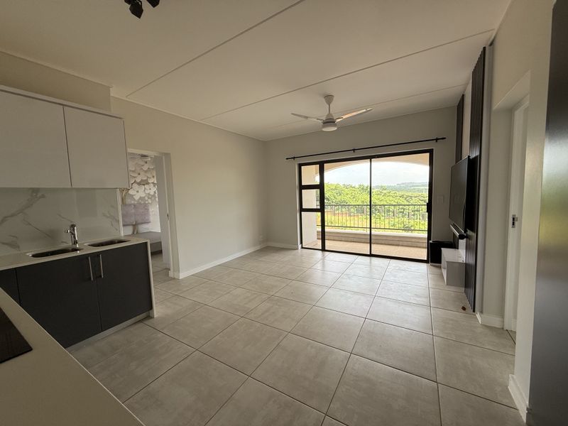 Spacious open-plan living area featuring modern kitchen cabinetry, tiled flooring, and a sliding door leading to a balcony with scenic views.