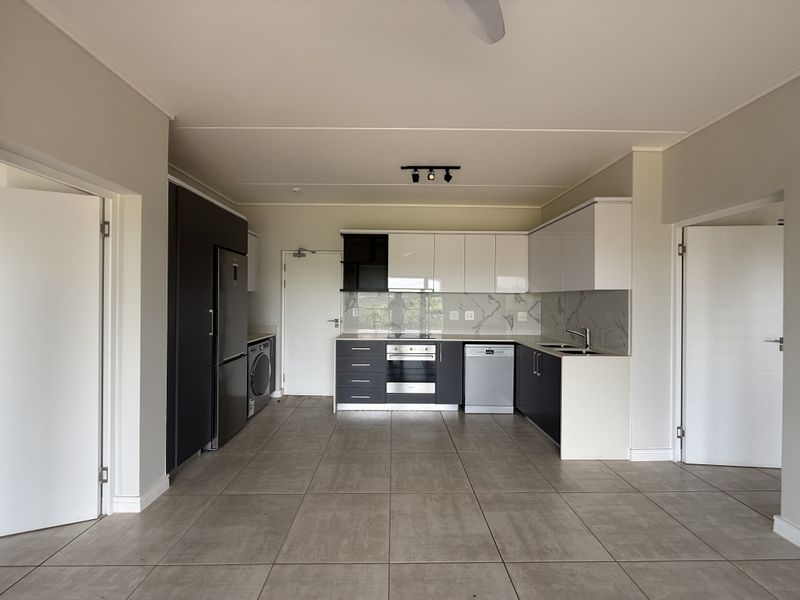 Modern open-plan kitchen featuring sleek two-tone cabinetry, stone countertops, integrated appliances, and large format floor tiles in a clean, contemporary space.