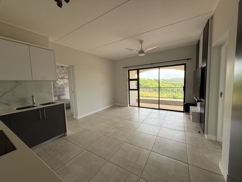 Modern open-plan living area featuring tiled floors, a sleek kitchen, and large sliding doors leading to a balcony with scenic views.