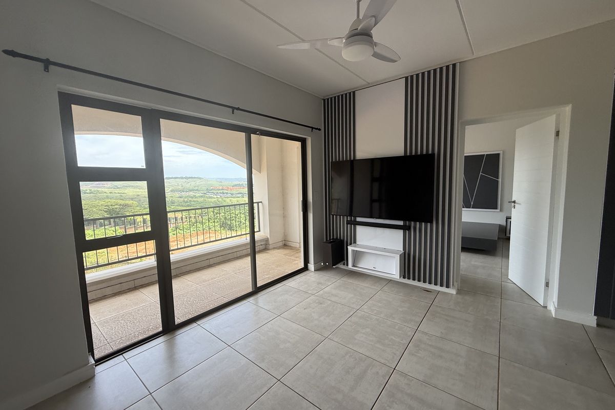 Modern living room featuring large sliding glass doors leading to a balcony, tiled flooring, and a decorative feature wall with integrated television mount.