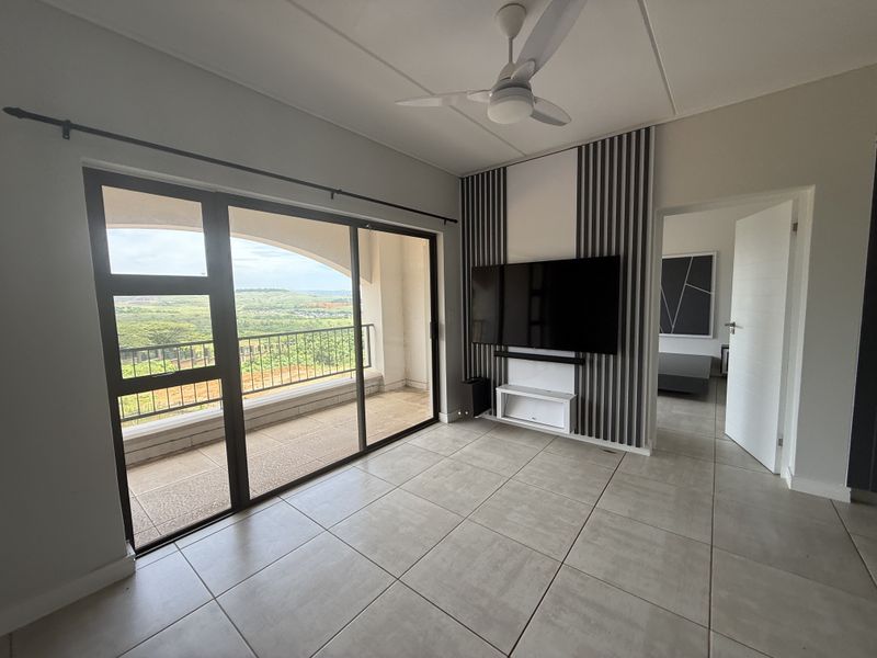 Modern living room featuring large sliding glass doors leading to a balcony, tiled flooring, and a decorative feature wall with integrated television mount.