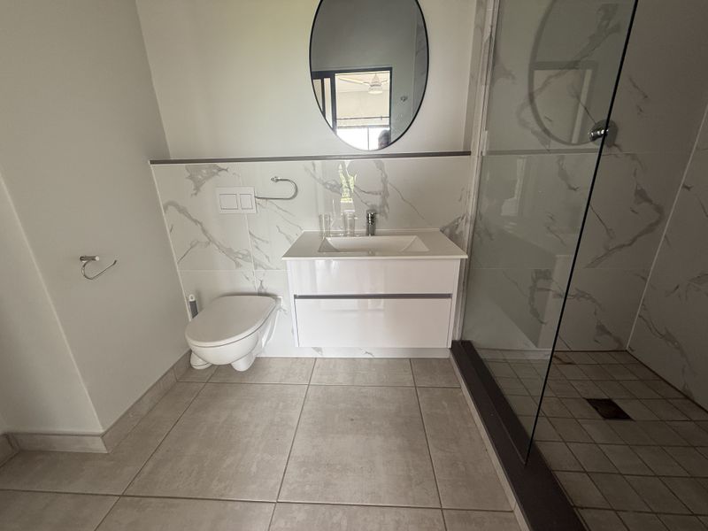 Modern bathroom featuring a wall-mounted toilet, vanity cabinet with integrated sink, and a spacious glass-enclosed shower with marble-look wall tiling.