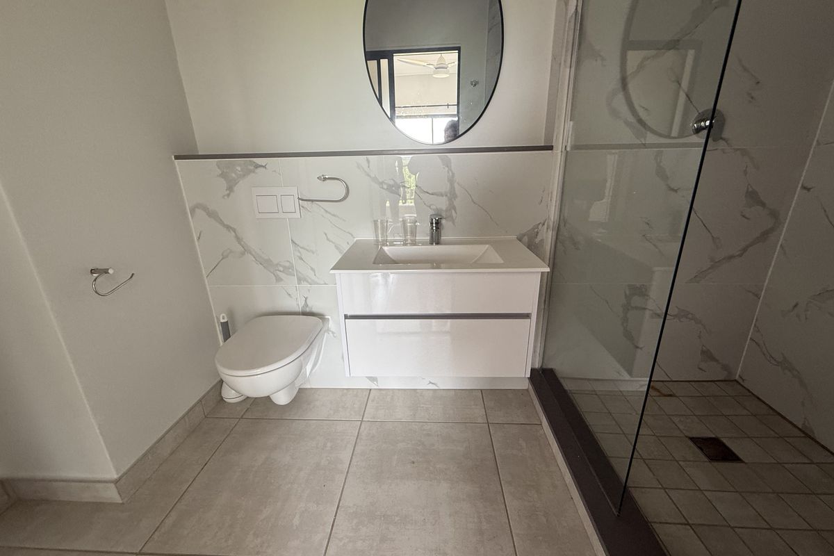 Modern bathroom featuring a wall-mounted toilet, vanity cabinet with integrated sink, marble-look wall tiling, and a glass-enclosed shower.