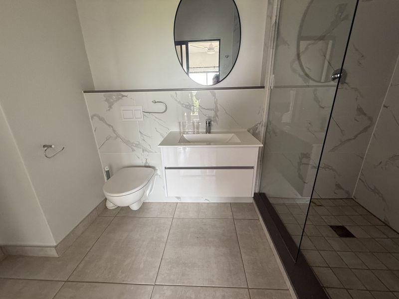Modern bathroom featuring a wall-mounted toilet, vanity cabinet with integrated sink, marble-look wall tiling, and a glass-enclosed shower.