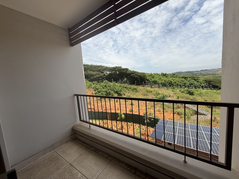 A covered balcony featuring tiled flooring, a metal balustrade, and an overhead louvre screen, offering an elevated view of the surrounding landscape.