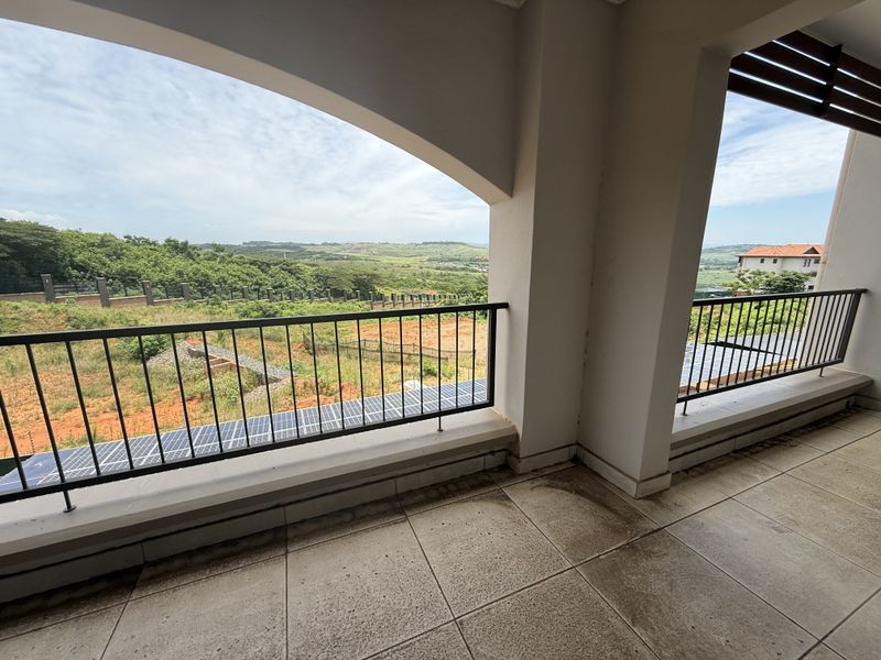 A covered balcony featuring metal balustrades and tiled flooring, offering expansive views of the surrounding landscape.