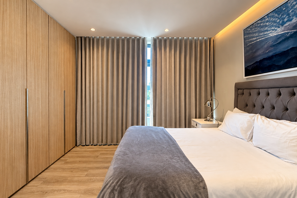 Modern bedroom featuring light wood built-in wardrobes, recessed ceiling lighting, cove accent lighting, and high-quality laminate flooring.