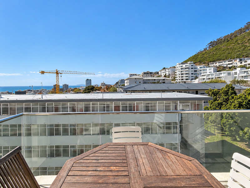 A balcony featuring a modern glass balustrade with a stainless steel handrail, offering expansive views of the surrounding neighborhood, mountain, and ocean.
