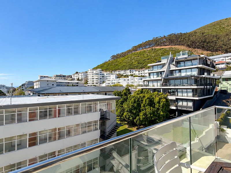 Elevated urban view overlooking surrounding apartment buildings and hillside landscape, featuring a modern glass balustrade with a stainless steel handrail.