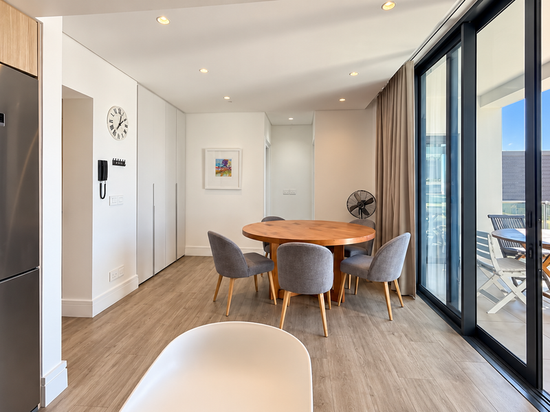 Modern open-plan living and dining area featuring light wood-look flooring, recessed lighting, and large sliding glass doors leading to a private balcony.