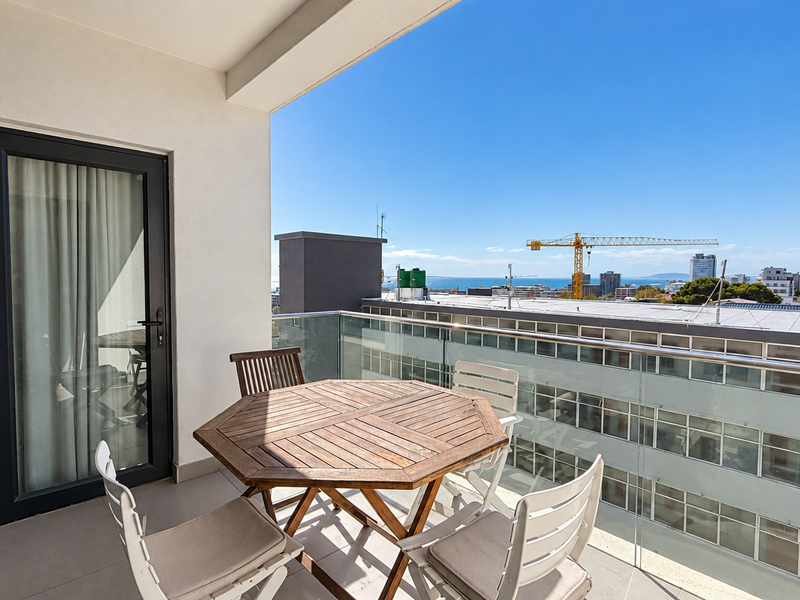 A modern balcony featuring a glass balustrade, tiled flooring, and a sliding door, offering an elevated urban view.