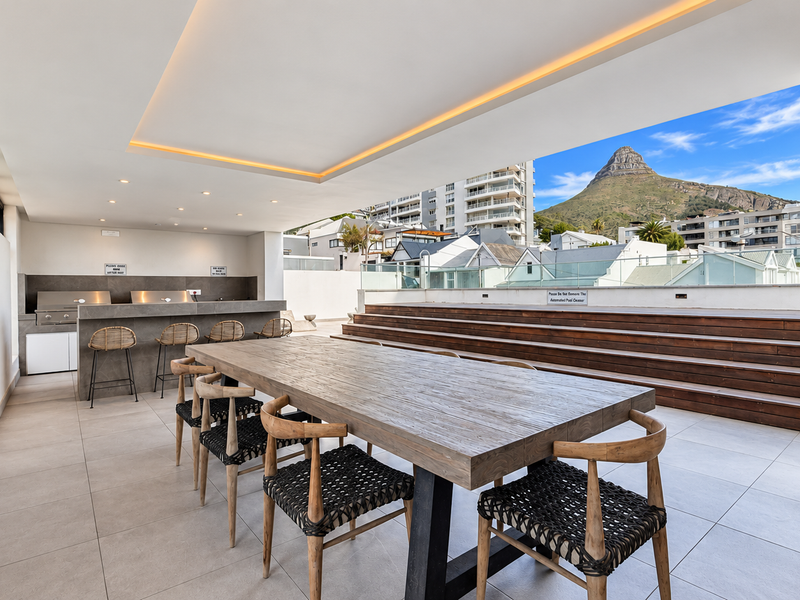 Spacious covered balcony featuring a built-in braai area, stone countertop, timber decking, and stunning mountain views, perfect for outdoor entertaining.