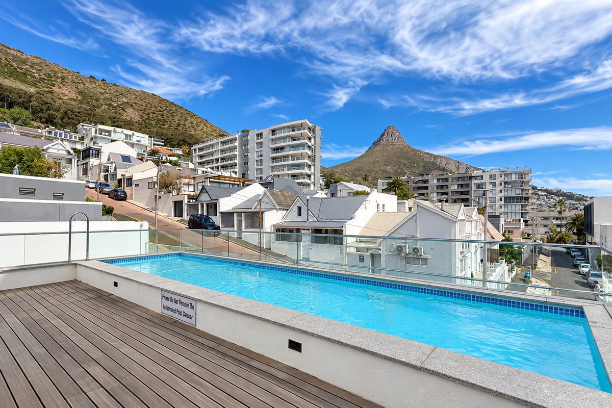 A modern elevated swimming pool featuring timber decking and a glass balustrade, offering scenic mountain and urban views.