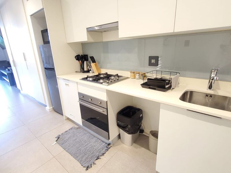 Modern kitchen featuring sleek white cabinetry, stone countertops, gas cooktop, built-in oven, and a glass splashback, seamlessly integrated into an open-plan living space.
