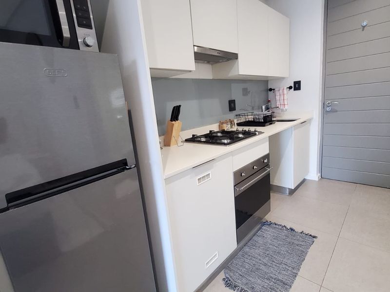 Modern kitchen featuring white cabinetry, stone countertops, glass splashback, gas hob, electric oven, and integrated stainless steel appliances with neutral tiled flooring.