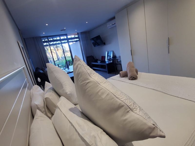 A well-lit bedroom featuring built-in cupboards, recessed lighting, and a sliding glass door providing access to an outdoor area.
