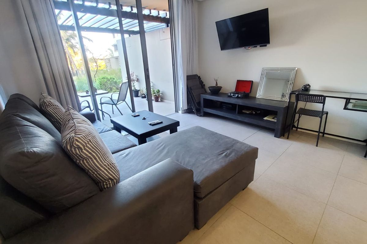 A bright living room featuring large sliding glass doors that open onto a patio, with neutral tiled flooring and a wall-mounted television.