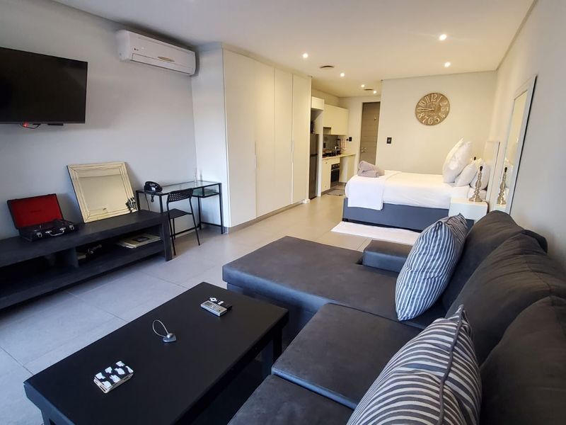 Modern open-plan studio apartment featuring a kitchenette, built-in storage, tiled flooring, and integrated air conditioning in a well-maintained living and sleeping space.